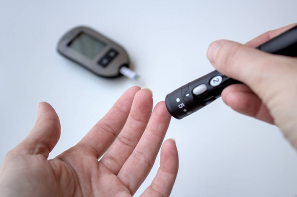 Тест на диабет. Пациент измеряет уровень глюкозы в крови, уколов палец дома. Клетчатый глюкометр - Фото, изображение