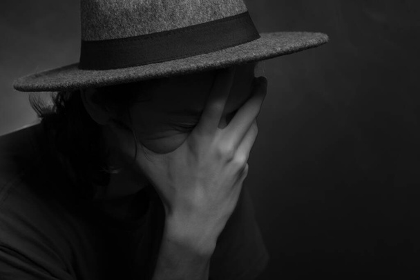 Close-up black and white portrait of thoughtful young man wearing hat. Isolated on smoky background. - Photo, image
