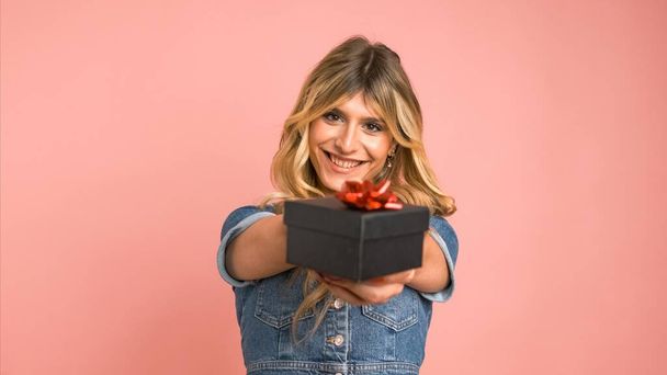 Happy transgender žena nabízí malé dárkové krabice při pohledu na kameru, jak stojí na růžovém pozadí - Fotografie, Obrázek