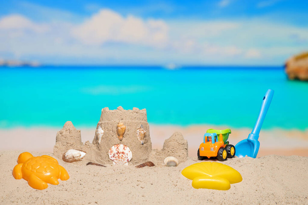 Piaszczysty zamek i zabawki dla dzieci na piaskowej plaży w tropikalnym kurorcie. Rodzinne wakacje. Relaks na pięknej plaży na wybrzeżu morza. Azure wody na oceanie, nadmorskim kurorcie. Wakacje. Błękitne niebo. Przestrzeń kopiowania. - Zdjęcie, obraz