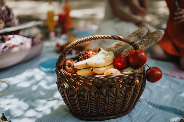 Ragazze che fanno un picnic all'aperto con un cesto pieno di frutta fresca, pane e verdure. Un rilassante e divertente raduno all'aperto sotto il sole. - Foto, immagini