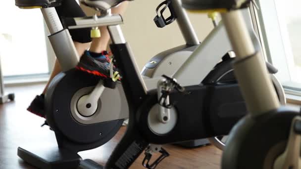 Νεαρός άνδρας περιστροφές πεντάλ στο ποδήλατο άσκησης στο σύγχρονο γυμναστήριο - Πλάνα, βίντεο