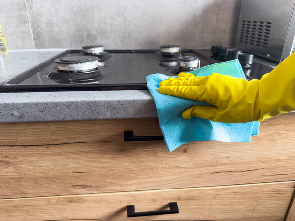  vrouw dragen gele handschoenen van een professionele schoonmaakbedrijf reinigt wast de keuken meubels - Foto, afbeelding