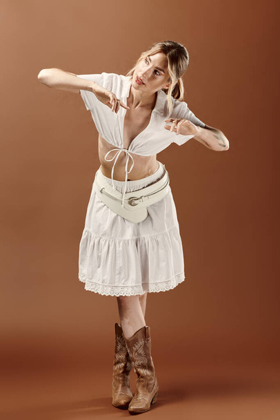 Mujer joven con vitiligo en conjunto de verano blanco y botas de vaquero golpeando una pose sobre un telón de fondo beige. - Foto, Imagen