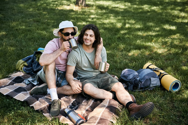 A young gay couple enjoys a break during their summer hike, sharing drinks and laughter in the peaceful wilderness. - Photo, Image