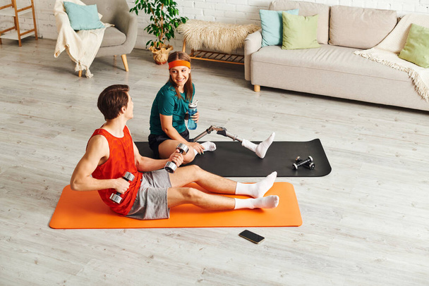 A couple exercises together in a living room. The woman has a prosthetic leg. - Photo, Image