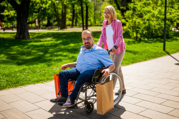 Ο ανάπηρος πάει από τα ψώνια. Ο φίλος του τον βοηθάει με την αναπηρική καρέκλα.. - Φωτογραφία, εικόνα