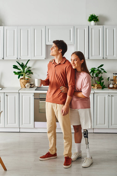 Couple in modern kitchen, woman with prosthetic leg, looking off-screen. - Foto, immagini