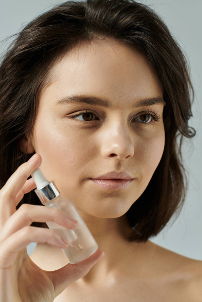 A close-up shot of a young woman holding a bottle of face serum in front of her face. - Foto, Imagen