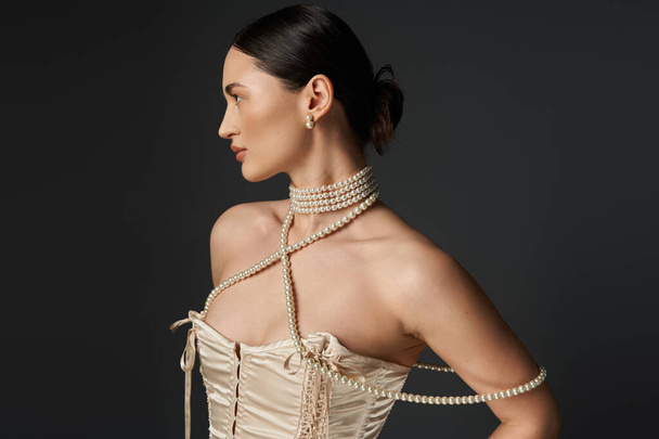 A young woman with brunette hair wears a pearl necklace and looks to the side against a dark background. - Foto, Imagem