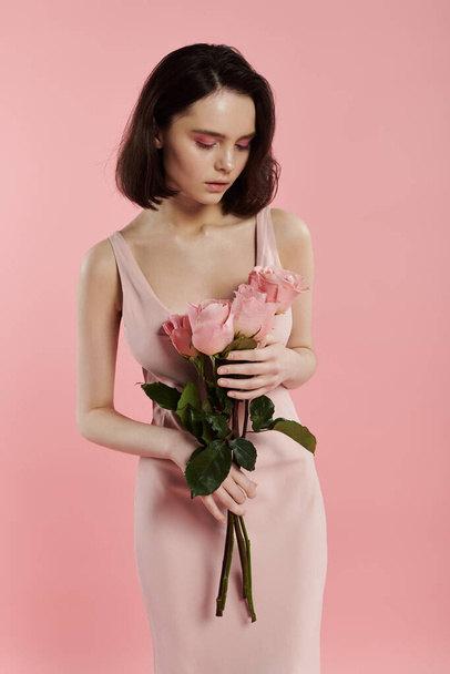 A woman in a pink dress holds a bouquet of roses in front of a bright pink background. - Фото, изображение