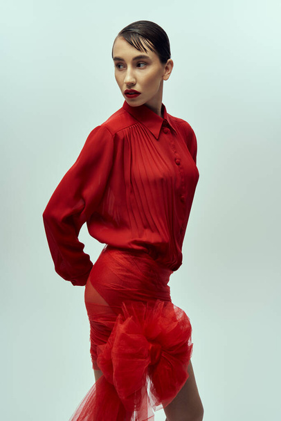 A young woman with short hair poses in a red dress against a grey background. - Fotó, kép