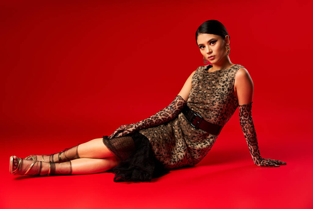 A young woman in a leopard print dress poses on a red backdrop. - Photo, Image