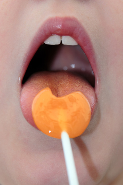オレンジ色のロリポップを舐める女の子 - 写真・画像