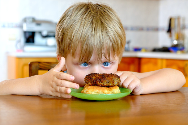Niño con chuleta en la cocina
 - Foto, Imagen