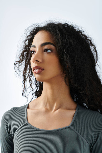 A young Black woman with curly hair looks off-camera while wearing a grey top. - Foto, immagini
