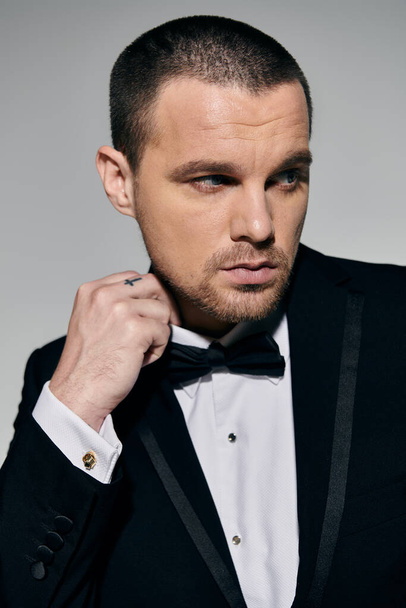A man in a tuxedo adjusts his bow tie, looking sharp and confident. - Foto, immagini