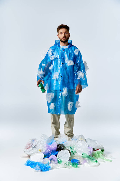 男はプラスチック廃棄物の山の上に立って,青いプラスチックのポンチョを着ています. - 写真・画像