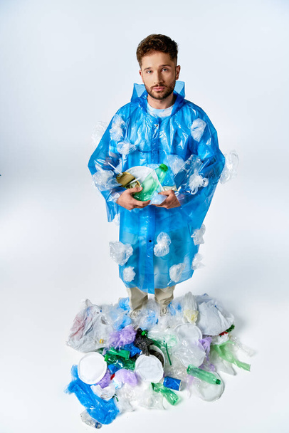 Egy férfi áll egy műanyag poncsóban, egy tengernyi műanyag hulladékkal körülvéve.. - Fotó, kép