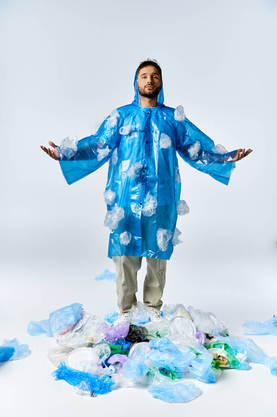 A man stands in a blue plastic raincoat on a pile of plastic waste. - Foto, Imagem