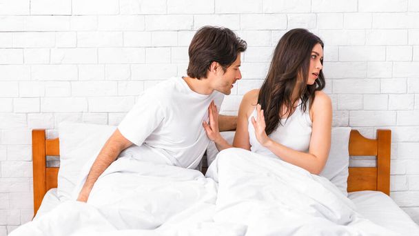 Genç bir çift sabahleyin yatakta tartışıyor. Erkek elini kadının göğsüne dayayıp öne doğru uzanıyor. Kadın da elini kaldırarak savunma yapıyor.. - Fotoğraf, Görsel