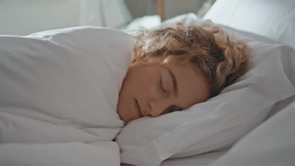 Tranquil woman sleeping pillow in morning. Carefree lazy girl hiding under blanket enjoying peaceful nap in cozy bedroom alone. Pretty curly model slumber dreaming on weekend. Tranquility at home. - Footage, Video