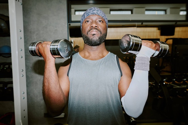 重いダンベルを持ち上げるアフリカ系アメリカ人男性,彼は運動技術に焦点を当てた - 写真・画像