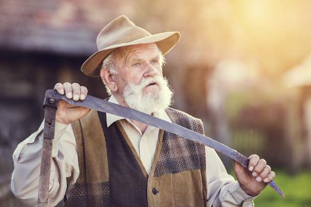 Old farmer with scythe taking a break - Foto, afbeelding
