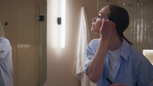 Relaxed girl applying mascara in bathroom mirror. Smiling woman admiring beauty doing stylish makeup closeup. Joyful happy lady looking reflection getting ready on weekend evening. Lifestyle concept. - Materiaali, video