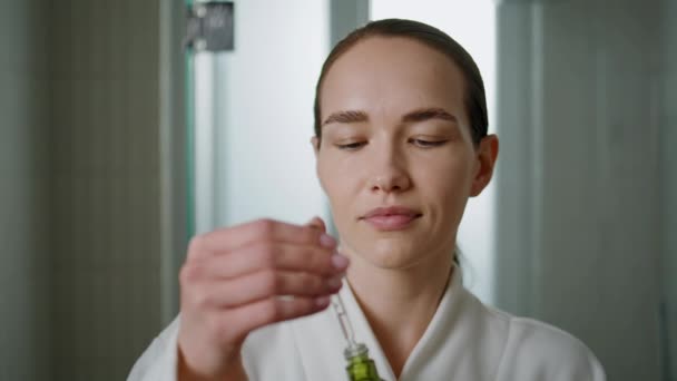 Closeup woman applying serum in morning bathroom. Smiling woman using dropper for facial moisturizing treatment. Serene pretty lady during skincare routine. Beauty product for skin health advertising. - Footage, Video
