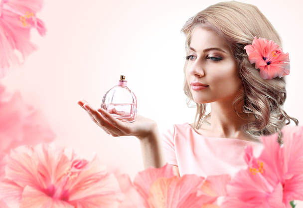 Beautiful woman with perfume bottle in flowers on pink background - Fotoğraf, Görsel