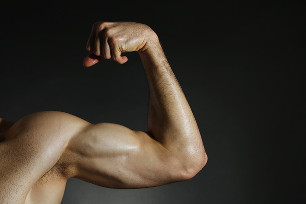 Muscular arm flexing on dark background - 写真・画像