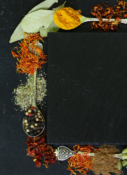 Verschillende kruiden op een zwarte achtergrond (paprika, kurkuma, peper, anijs, kaneel, saffraan) - Foto, afbeelding