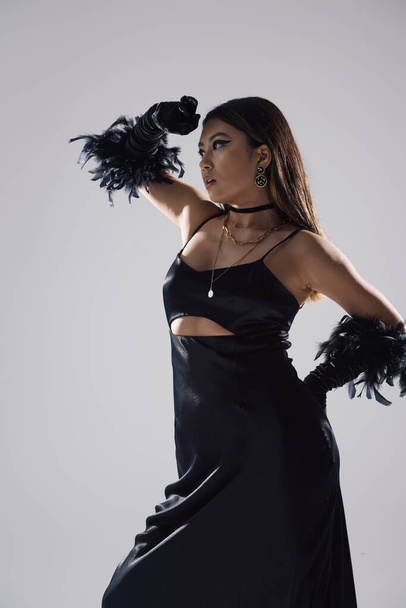 An Asian woman in a black dress and feather gloves, poses dramatically against a white background. - Foto, immagini