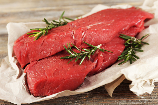 Raw beef steak with rosemary on paper on wooden background - Foto, Bild