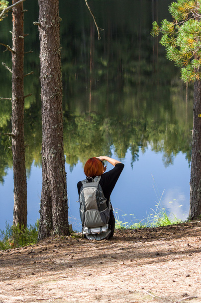 Turista mujer fotografiando un lago de bosque con reflejo
 - Foto, imagen