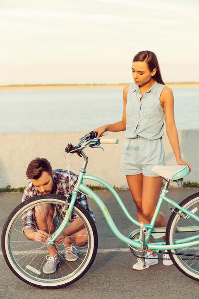 Frustrated woman with bicycle and man repairing wheel - Foto, Imagem