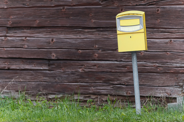 Традиционный желтый почтовый ящик перед деревянной стеной
 - Фото, изображение