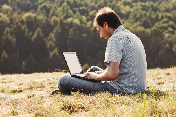 Young man using laptop sitting on the grass on the hillside - Photo, Image
