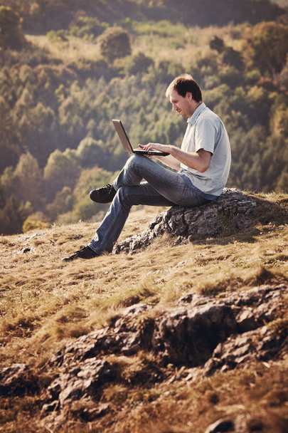 fiatal ember használ laptop ül a fűben, a hegyoldalban - Fotó, kép