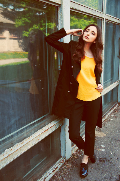 junges Frauenporträt in schwarzem Trenchcoat und gelber Bluse - Foto, Bild
