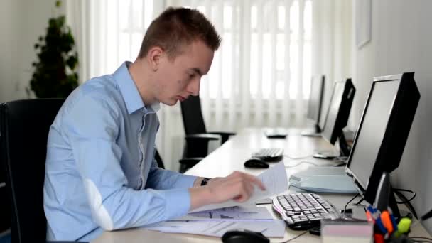fiatal jóképű férfi dolgozik asztali számítógép és olvassa dokumentum az irodában - Felvétel, videó