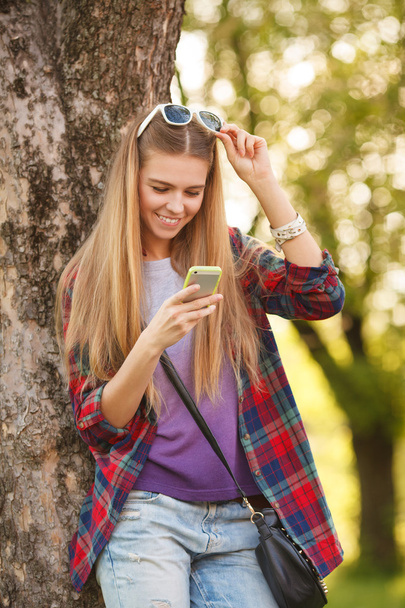 Усміхнена дівчина друкує на мобільному телефоні
 - Фото, зображення
