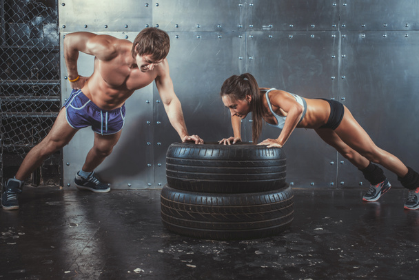 Des sportives. Fit femme sportive et l'homme faisant des pompes sur la force des pneus concept d'entraînement de puissance Crossfit fitness entraînement sport style de vie
. - Photo, image