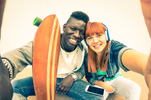 Hipster-Paar mit mehreren Rassen beim Selfie auf weißem Hintergrund - lustiges Konzept mit alternativen Mode- und Technologietrends - rothaarige Freundin mit afroamerikanischem Kerl - Vintage-Filterlook - Foto, Bild