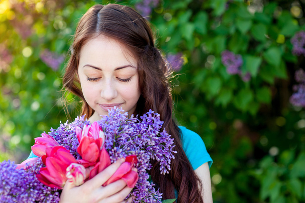 Beautiful girl with a bouquet of lilac in hands walking at spring park - Foto, Imagem