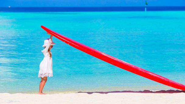 Tropikal beyaz plaj üzerinde kırmızı büyük surfboard ile sevimli küçük kız - Fotoğraf, Görsel