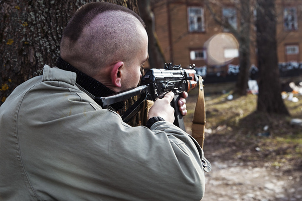 Een mannelijke met het pistool skinhead dreigt te iemand achter de bomen - Foto, afbeelding