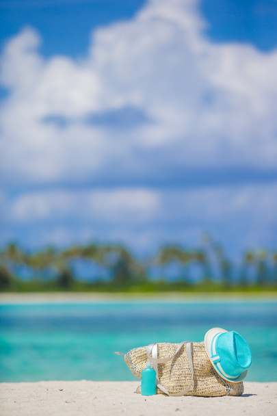 Bolsa de paja, sombrero azul, gafas de sol y botella de protector solar en la playa tropical
 - Foto, imagen