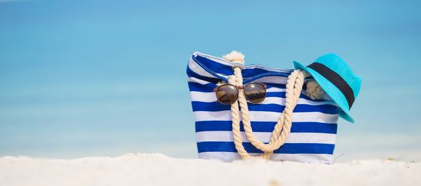 Εξαρτήματα παραλιών - μπλε τσάντα, ψάθινο καπέλο, γυαλιά ηλίου σε παραλία με λευκή - Φωτογραφία, εικόνα